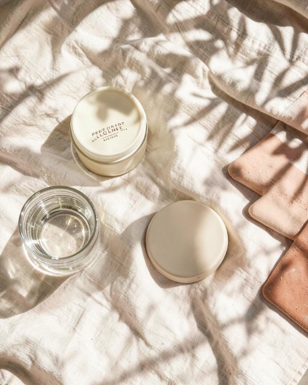 Morning wellness routine on warm linen with water and a cream jar